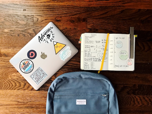 blue backpack beside a book and a silver MacBook laptop