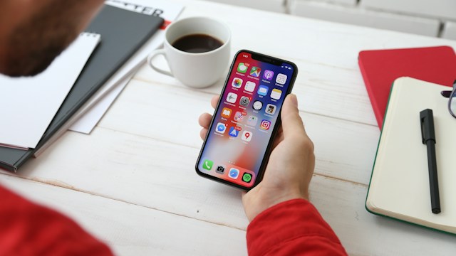 person holding a gray iPhone X with apps showing on the screen